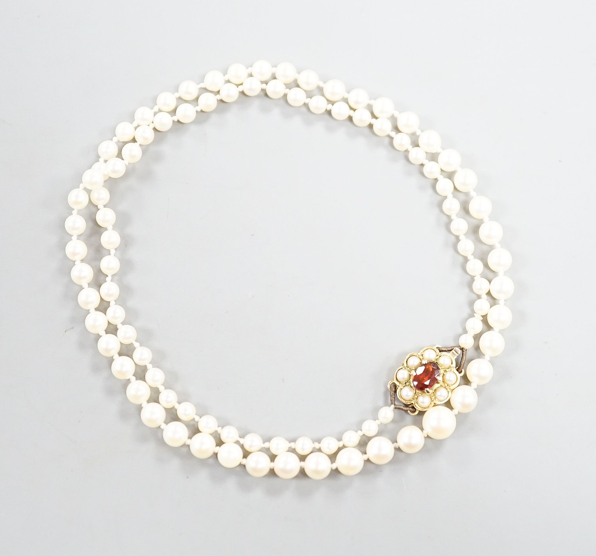 A single strand graduated cultured pearl necklace, with 9ct, garnet and cultured pearl cluster set clasp, 53cm.